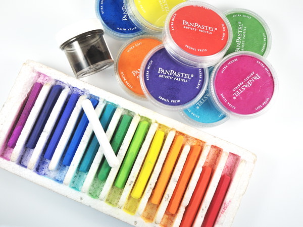 Brightly colored soft pastel sticks in an array, along with round containers of brightly colored Pan Pastels.