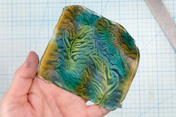 A hand holding a sheet of polymer clay that was textured and then colored with pastels.