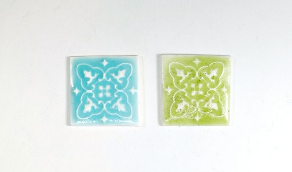 Two square polymer clay tiles that have had a faux ceramic effect applied by using pastels and liquid polymer clay.