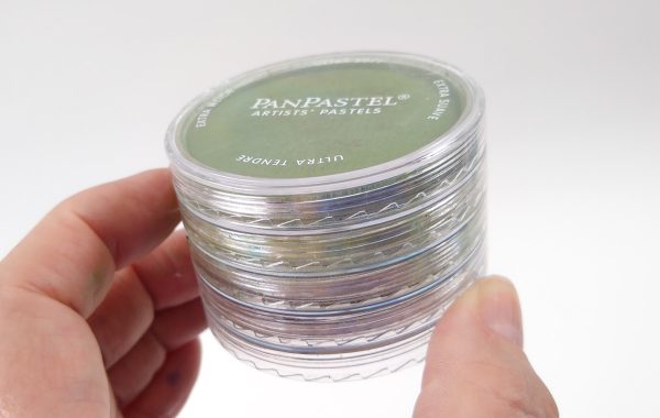 A hand holding a stack of Pan Pastel containers.