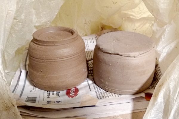 Two wheel-thrown ceramic pots, greenware, inverted on newspaper to dry.