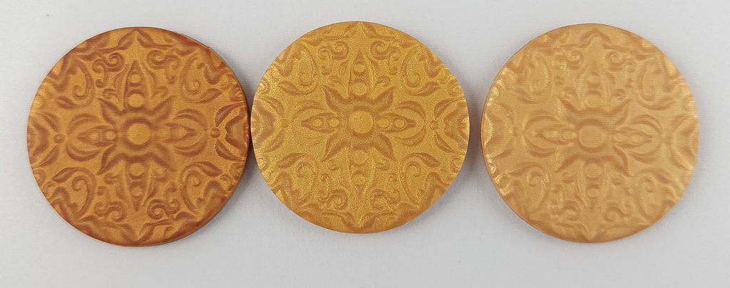 Three circles of gold polymer clay, showing the difference between the mica shift and color of Premo vs Du-kit.