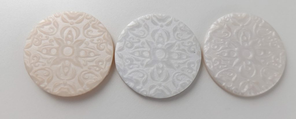 Three circles of pearl colored polymer clay showing mica shift, comparing three brands.