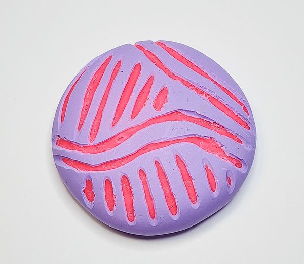 Lilac colored dome of Du-kit polymer clay that has been carved to reveal a hot pink design.
